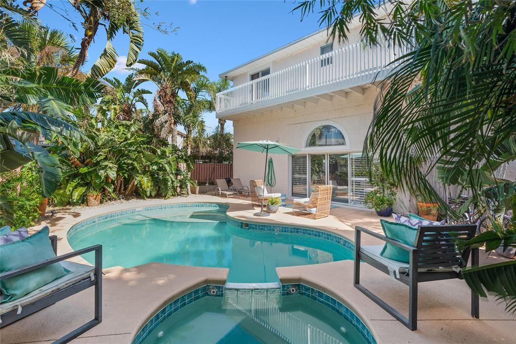A backyard features a swimming pool, a hot tub, patio furniture, and lush tropical landscaping — 1422 N ATLANTIC AVENUE, NEW SMYRNA BEACH, FL