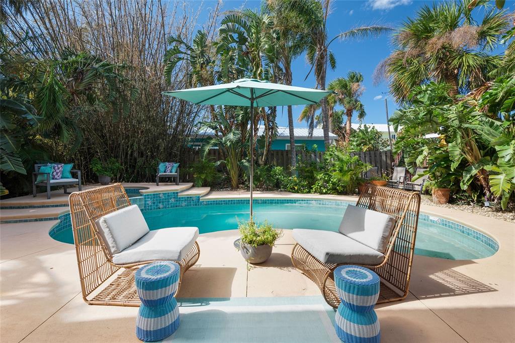 A backyard patio features two wicker chairs, blue stools, and an umbrella by a pool — 1422 N ATLANTIC AVENUE, NEW SMYRNA BEACH, FL