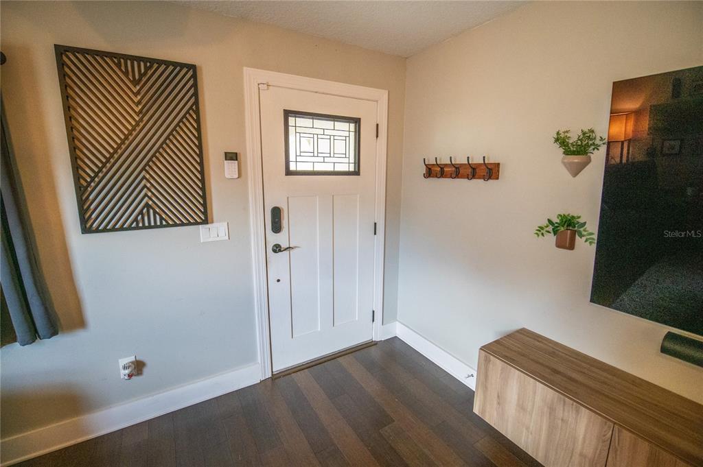 An entryway features a white front door, dark wood flooring, wall art, and coat hooks — 2429 S BROWN AVENUE, ORLANDO, FL
