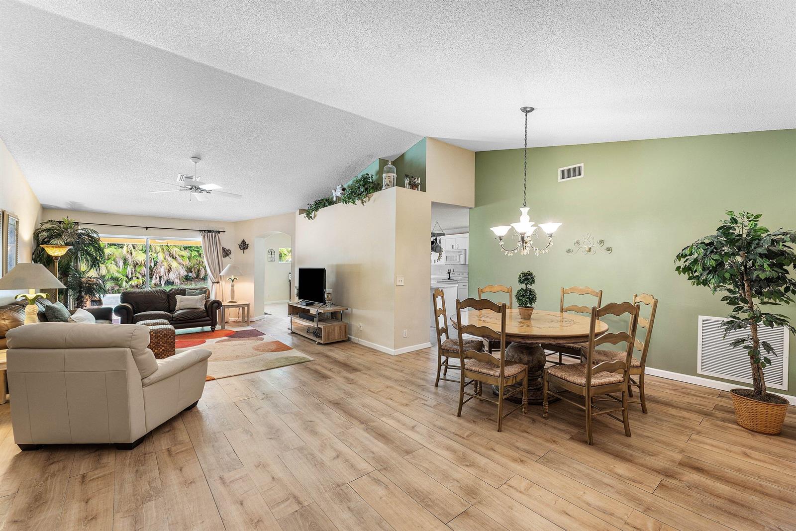 A living and dining room with wood-look flooring, vaulted ceilings, and a green accent wall — 4824 S Lee Road, Delray Beach FL 33445, DELRAY BEACH, FL