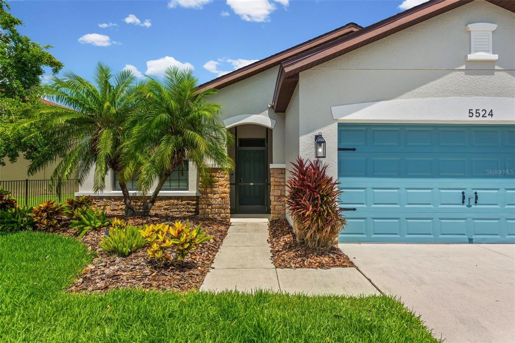 The exterior of a single-story house features a blue garage door and a stone-accented entryway — 5524 107TH TERRACE E, PARRISH, FL