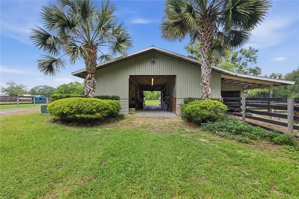 An exterior view of a light green barn with two palm trees and fenced paddocks — 5999 NW 90TH AVENUE, OCALA, FL