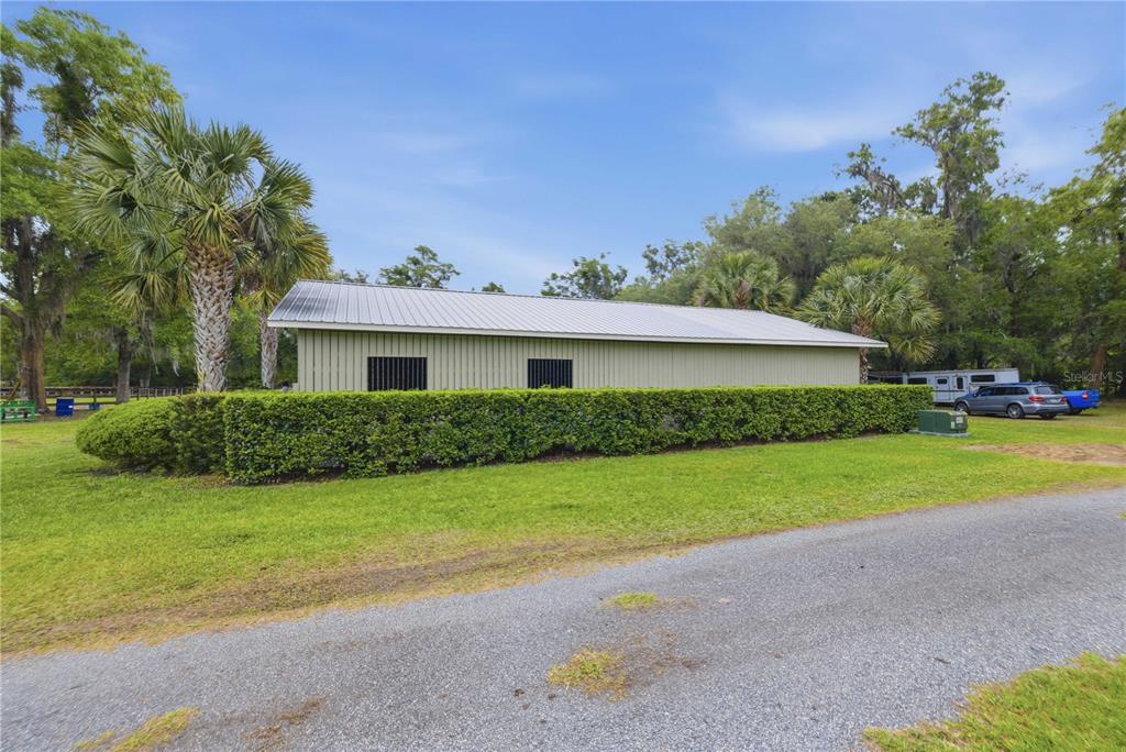 A light green metal building with a metal roof sits behind a manicured hedge — 5999 NW 90TH AVENUE, OCALA, FL