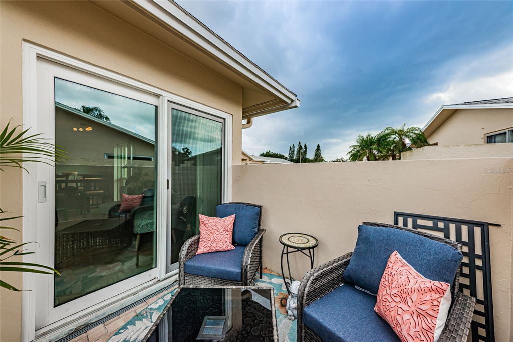 A patio features two wicker chairs with blue cushions and pink pillows near a sliding door — 2735 SHERBROOKE LANE UNIT C, PALM HARBOR, FL