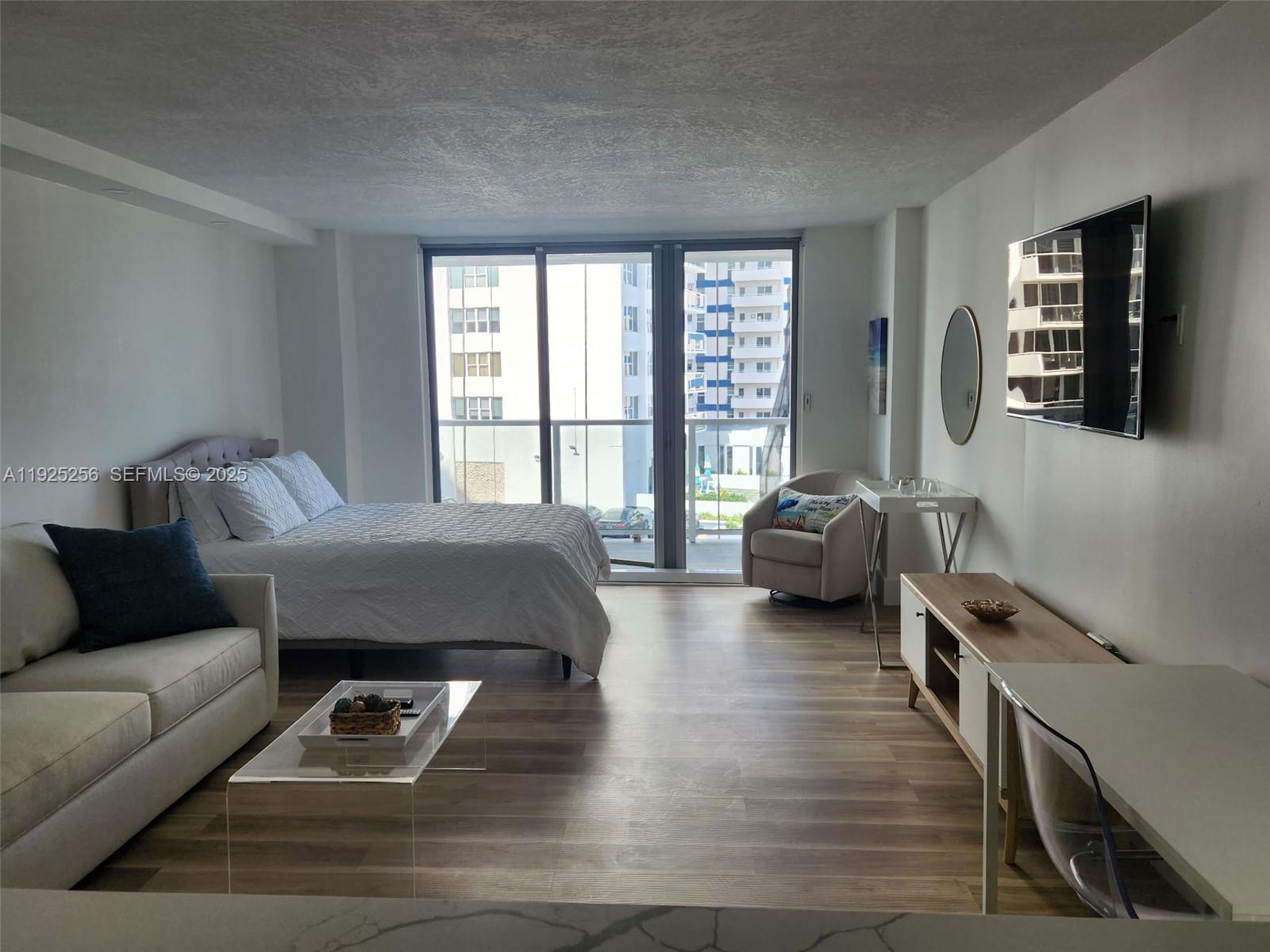 A studio apartment features a bed, sofa, television, and a balcony with city views — 3180 S Ocean Dr # 307, Hallandale Beach FL 33009, HALLANDALE BEACH, FL