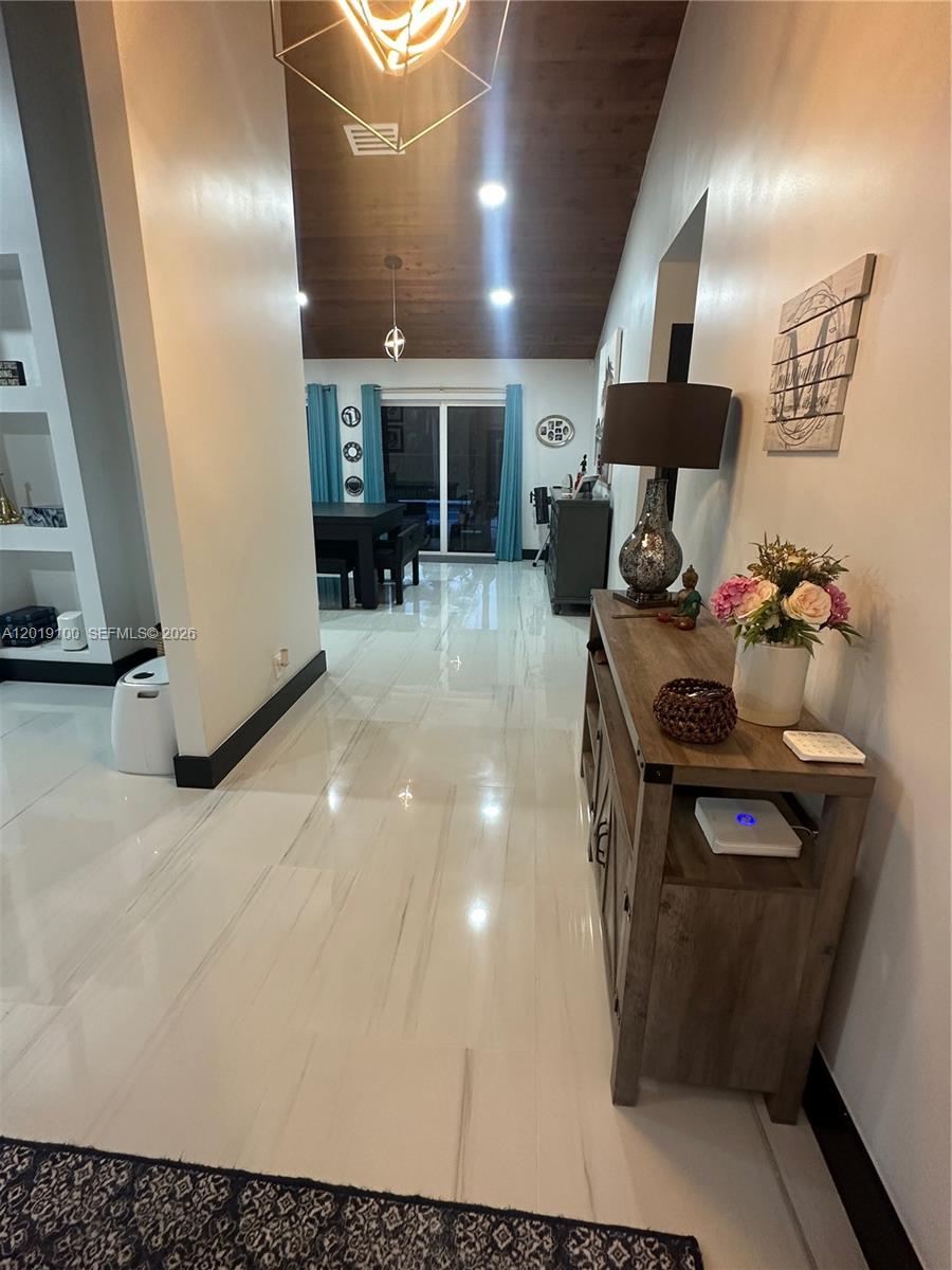 A hallway with white marble-look tile floors leads toward a dining area with vaulted ceilings — 11701 SW 21st Ct, Davie FL 33325, DAVIE, FL