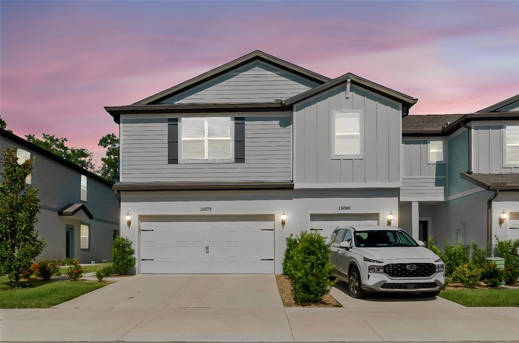 A two-story duplex with gray siding, white stucco, and a white car in the driveway — 13078 STILLMONT PLACE, TAMPA, FL