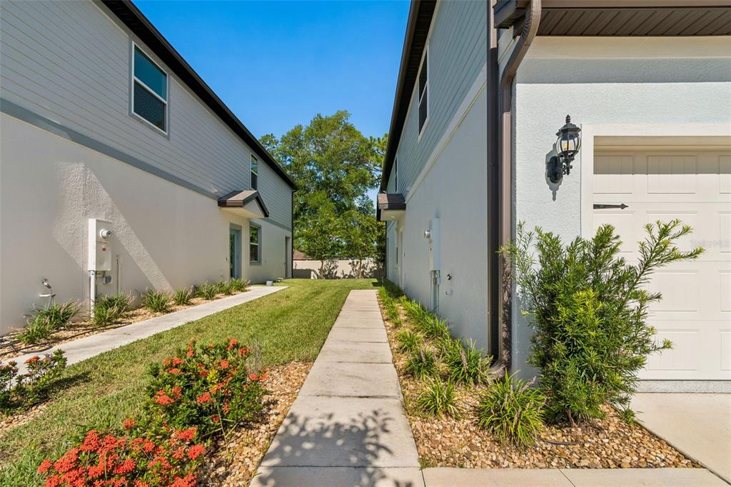 A narrow grassy walkway sits between the side walls of two adjacent suburban residential buildings — 13078 STILLMONT PLACE, TAMPA, FL