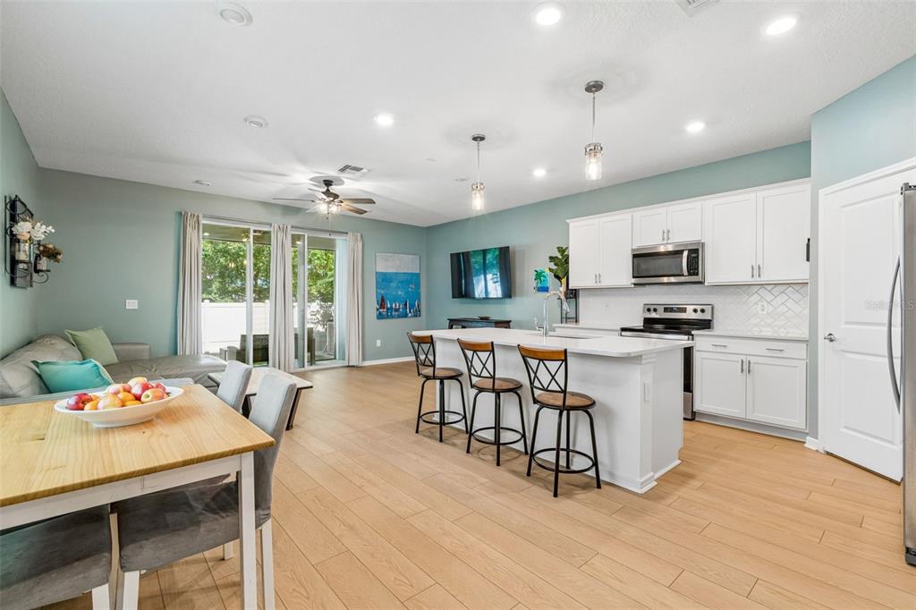 An open-concept kitchen and living area featuring white cabinets, a central island, and wood flooring — 13078 STILLMONT PLACE, TAMPA, FL