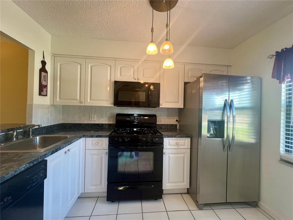 A kitchen with white cabinets, dark countertops, black appliances, and a stainless steel refrigerator — 2989 FLINT DRIVE N, CLEARWATER, FL