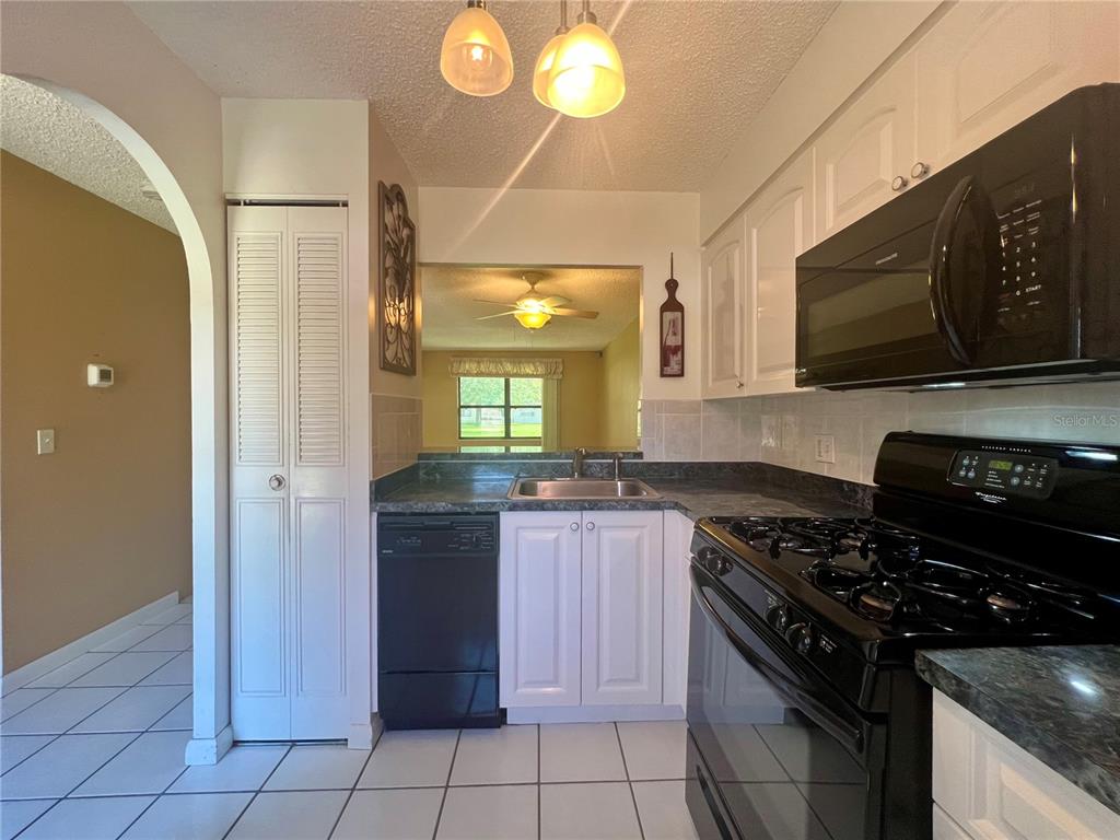 A kitchen features white cabinets, black appliances, a tiled floor, and a pass-through window — 2989 FLINT DRIVE N, CLEARWATER, FL