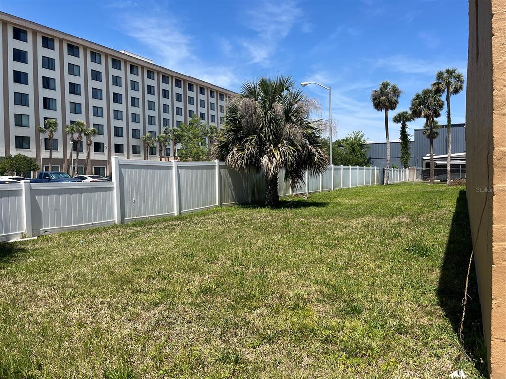A grassy backyard features a white vinyl fence, a large palm tree, and a hotel building — 112 FAIRVIEW AVENUE, DAYTONA BEACH, FL