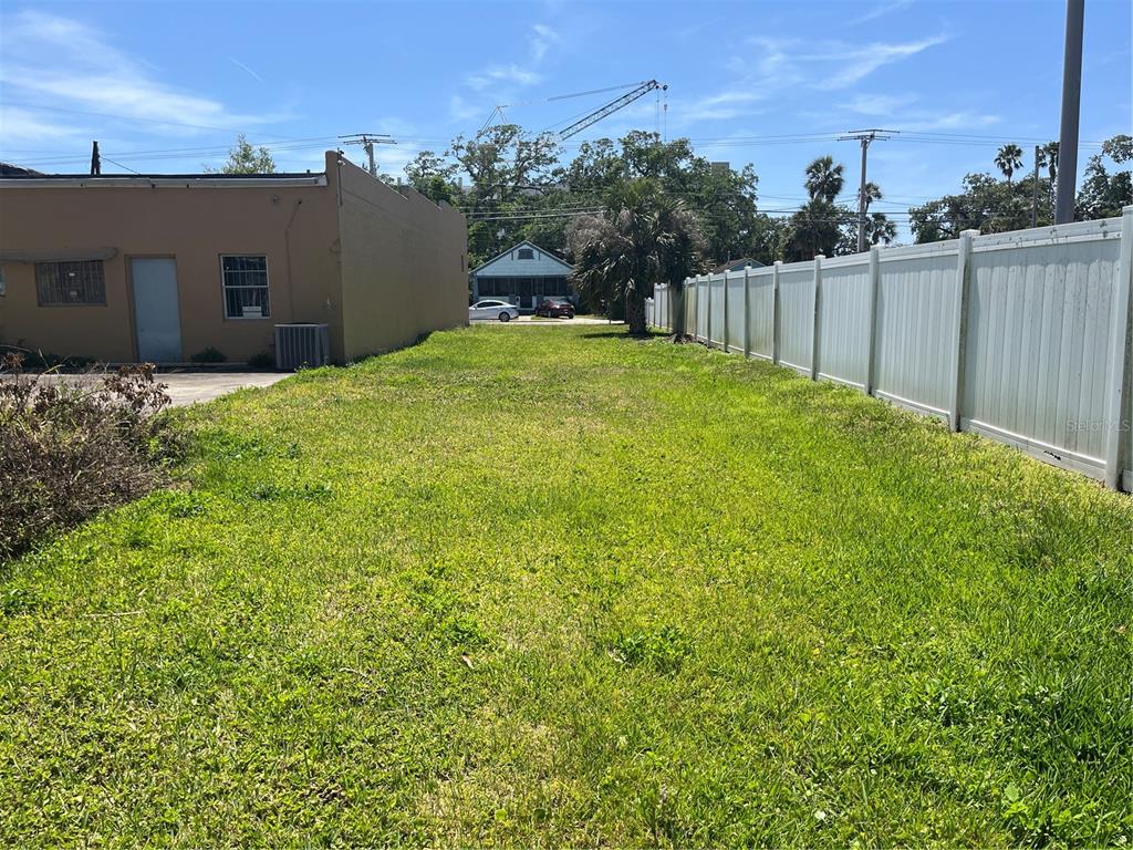A grassy vacant lot sits between a tan building and a white vinyl fence — 112 FAIRVIEW AVENUE, DAYTONA BEACH, FL