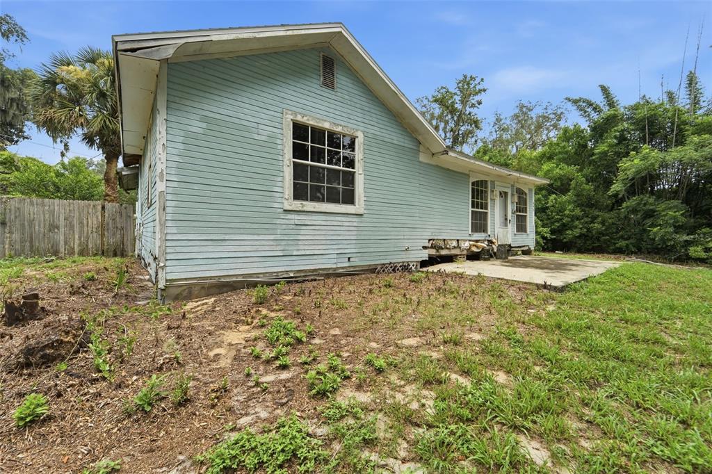 The exterior of a light blue house with a concrete patio and overgrown yard — 495 NORTH STREET, DE LEON SPRINGS, FL