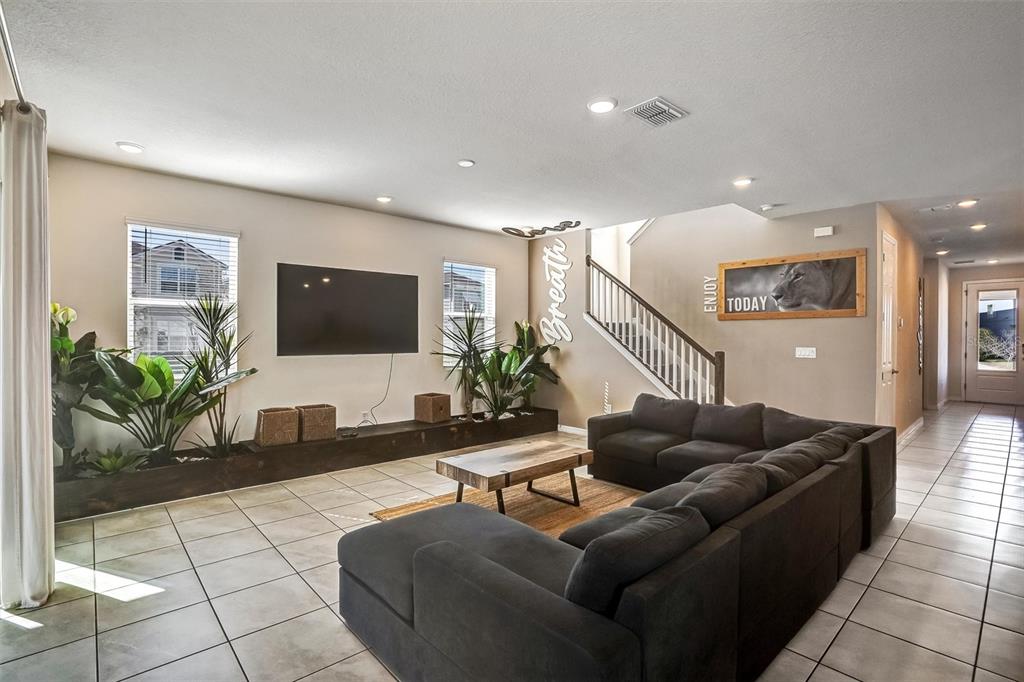 A living room features a large sectional sofa, a wall-mounted television, and a staircase — 8918 TROPICAL HAVEN COURT, KISSIMMEE, FL