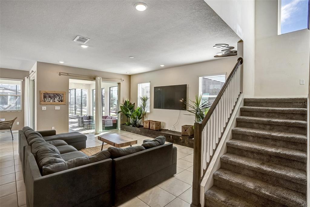 A living room features a grey sectional sofa, a wall-mounted television, and a carpeted staircase — 8918 TROPICAL HAVEN COURT, KISSIMMEE, FL