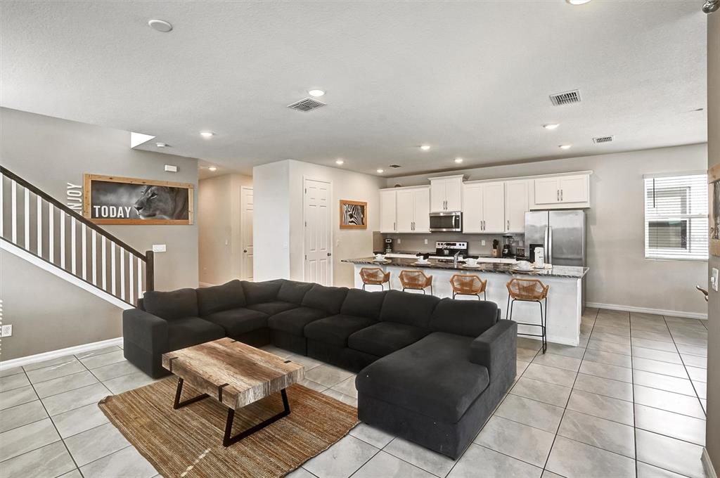 An open-concept living room features a large black sectional, a wooden coffee table, and a kitchen — 8918 TROPICAL HAVEN COURT, KISSIMMEE, FL