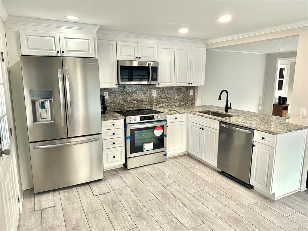 A kitchen with white cabinets, stainless steel appliances, granite countertops, and light wood-look flooring — 9790 66TH STREET N UNIT 37, PINELLAS PARK, FL