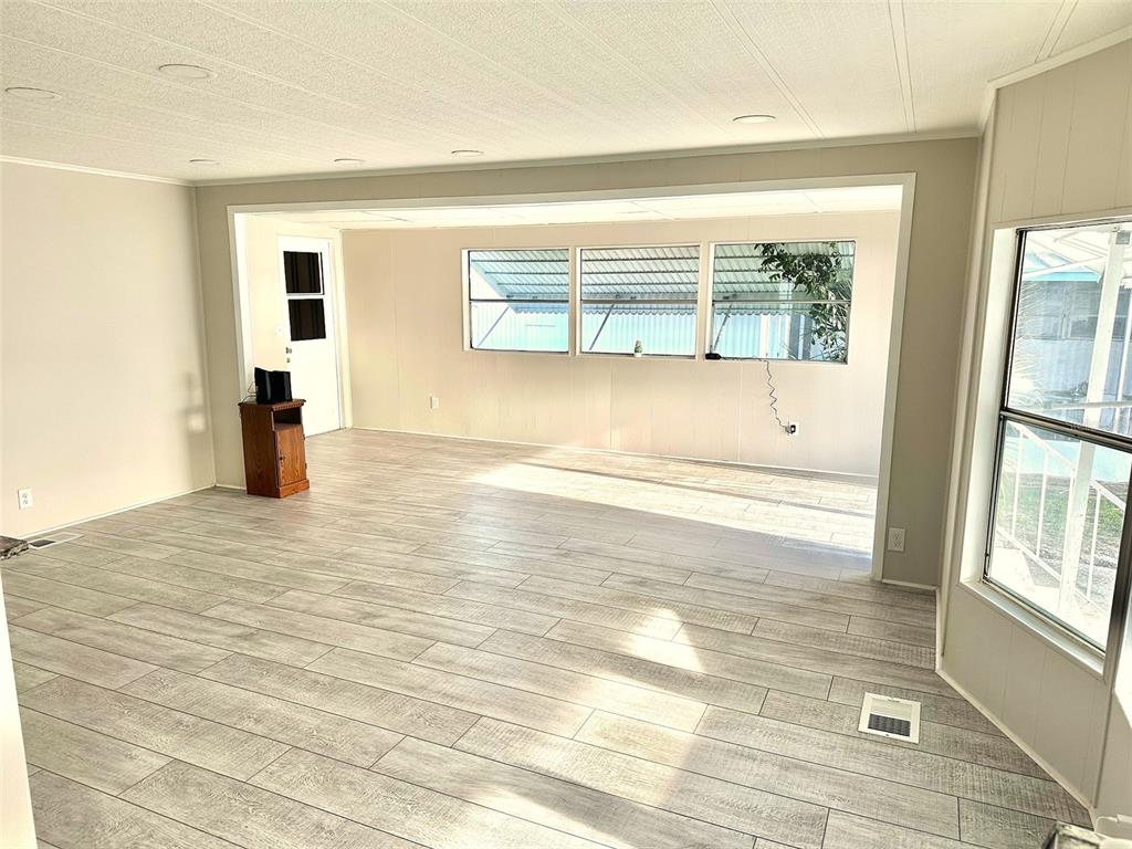 A living room with light wood-look flooring, white walls, and a large windowed sunroom area — 9790 66TH STREET N UNIT 37, PINELLAS PARK, FL