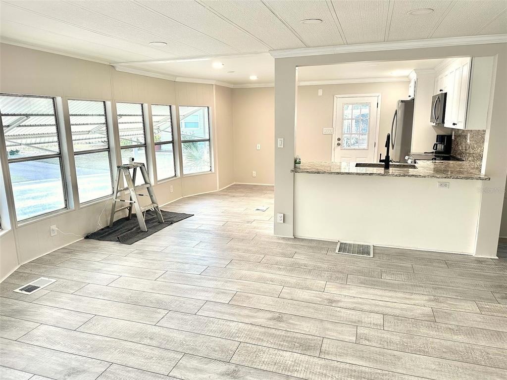 A living area with light wood-look flooring leads to a kitchen with granite countertops — 9790 66TH STREET N UNIT 37, PINELLAS PARK, FL