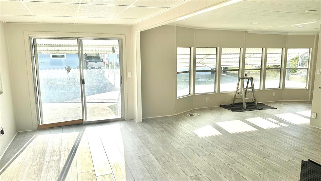 A bright room with light wood-look flooring, large windows, and sliding glass doors — 9790 66TH STREET N UNIT 37, PINELLAS PARK, FL