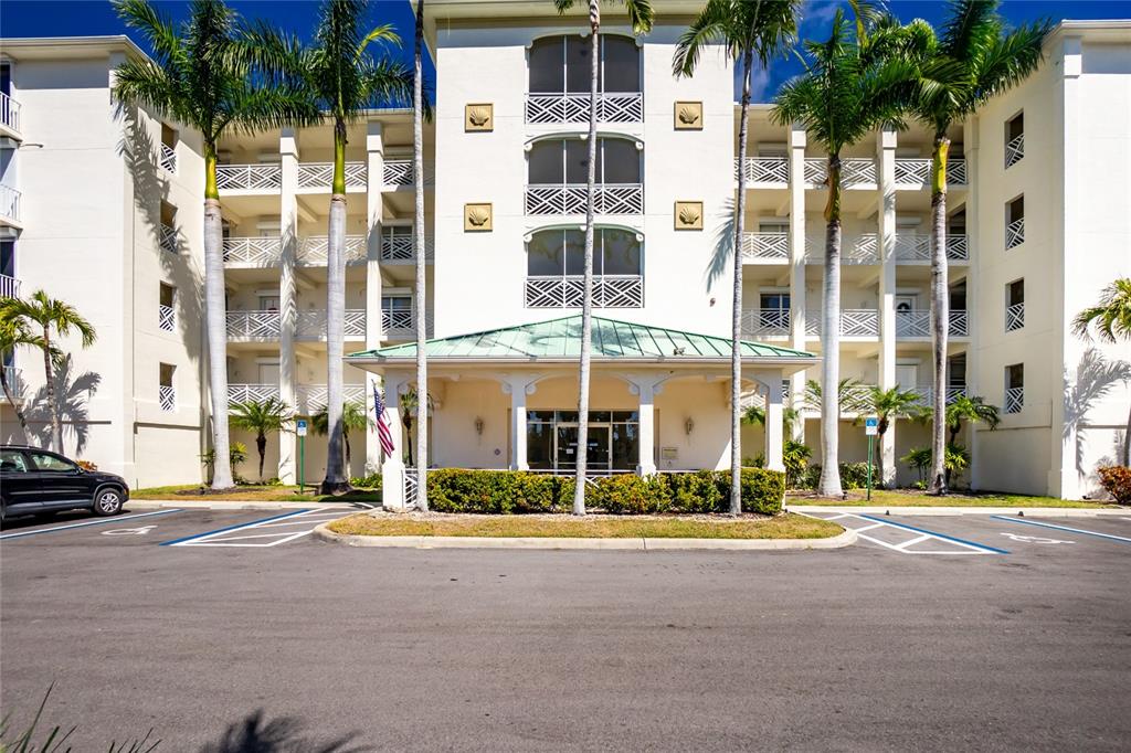 The exterior of a multi-story building features a covered entrance, palm trees, and parking spaces — 200 HARBOR WALK DRIVE UNIT 353, PUNTA GORDA, FL