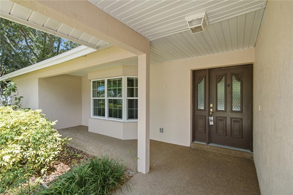 A covered entryway features a brown double door, a bay window, and a concrete porch — 9743 106TH AVENUE, LARGO, FL