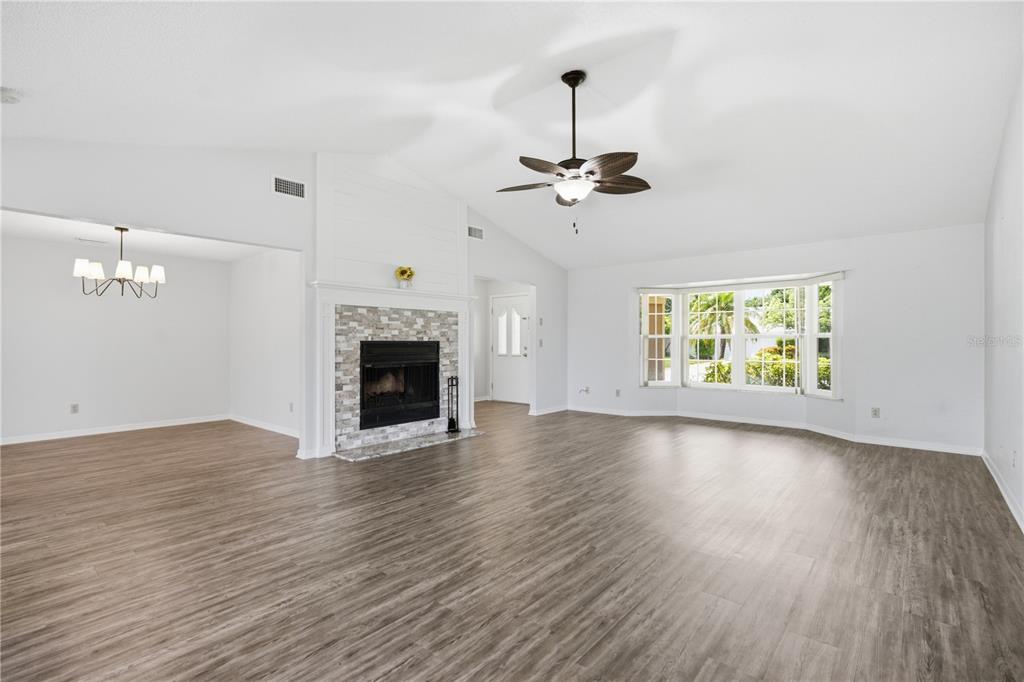 A living room features wood-look flooring, a stone fireplace, a ceiling fan, and bay windows — 9743 106TH AVENUE, LARGO, FL