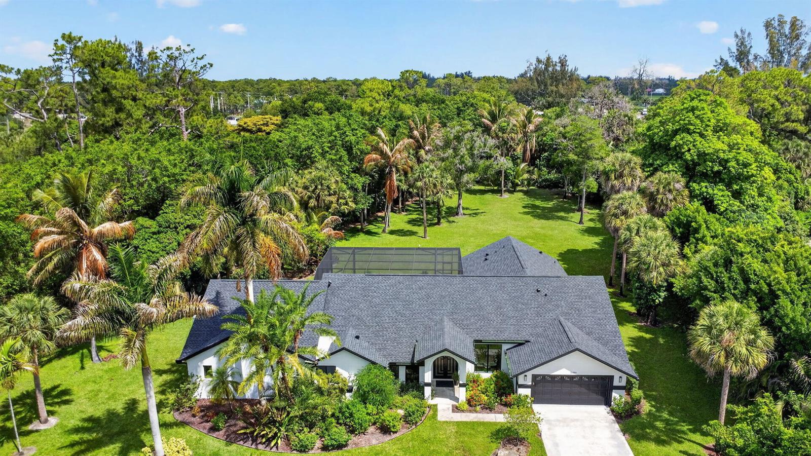 An aerial view of a white house with a dark roof, pool cage, and surrounding trees — 13399 Doubletree Circle, Wellington FL 33414, WELLINGTON, FL