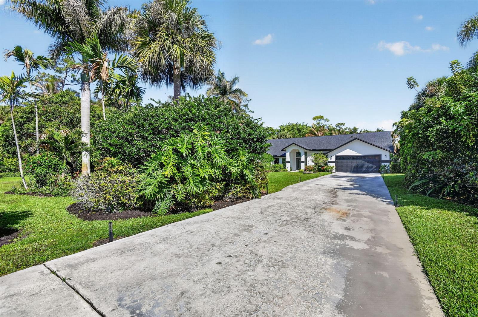 A long concrete driveway leads to a single-story house surrounded by lush tropical landscaping — 13399 Doubletree Circle, Wellington FL 33414, WELLINGTON, FL