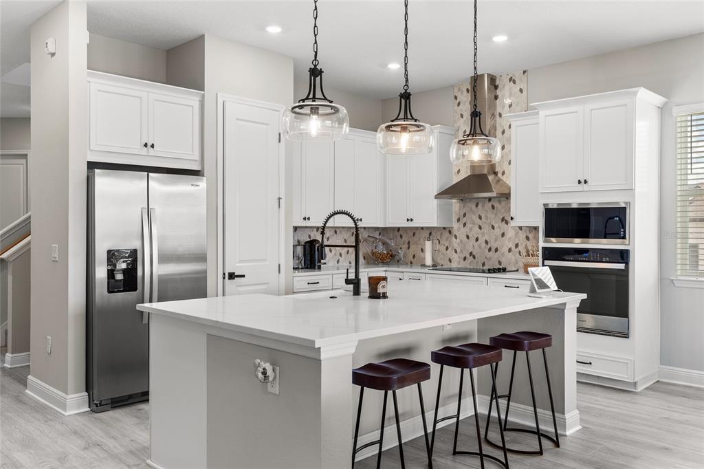 A modern kitchen features white cabinets, a large quartz island, stainless steel appliances, and pendant lighting — 6515 QUEST STREET, ST CLOUD, FL