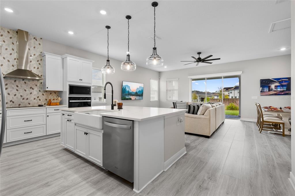 A modern kitchen with white cabinetry and a large island opens to a living area — 6515 QUEST STREET, ST CLOUD, FL