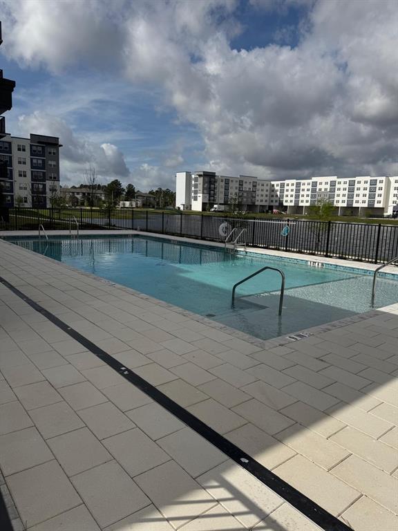 An outdoor swimming pool with a tanning ledge overlooks a lake and large apartment buildings — 5579 MILLENIA PARK BOULEVARD UNIT 506, ORLANDO, FL