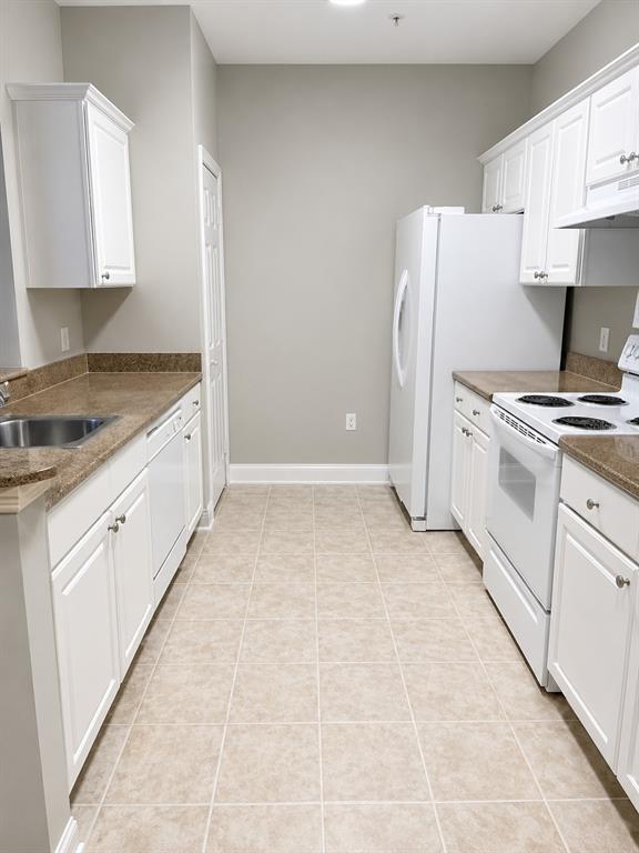 A galley kitchen features white cabinets, brown countertops, and white appliances on a tiled floor — 303 SOUTHERN PECAN CIRCLE UNIT 107, WINTER GARDEN, FL