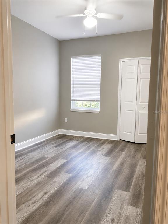 An empty bedroom features light gray walls, wood-look flooring, a ceiling fan, and a closet — 303 SOUTHERN PECAN CIRCLE UNIT 107, WINTER GARDEN, FL