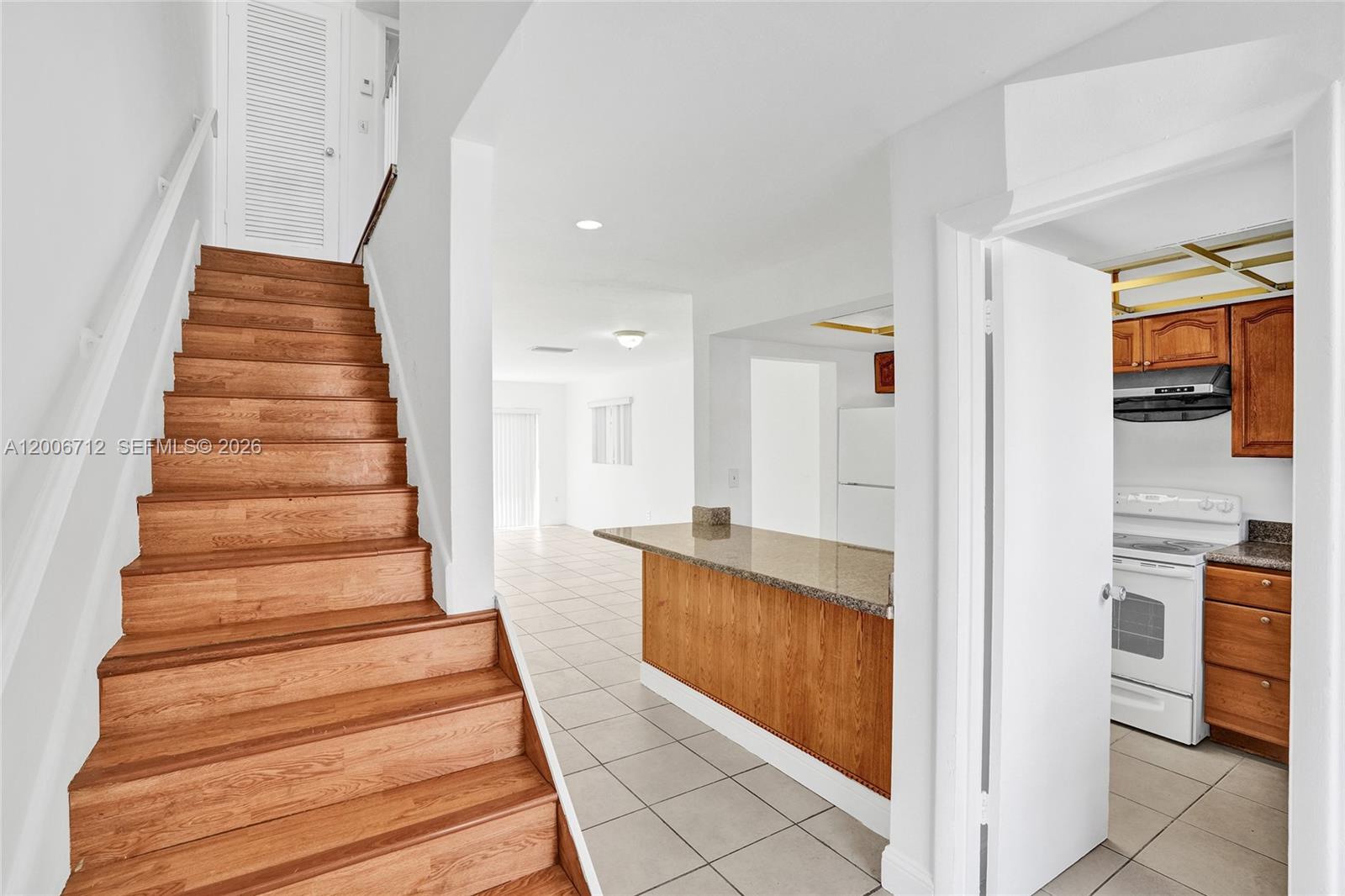 A wooden staircase leads upward next to a kitchen with wood cabinets and tile floors — 7344 SW 82nd St # C114, Miami FL 33143, MIAMI, FL