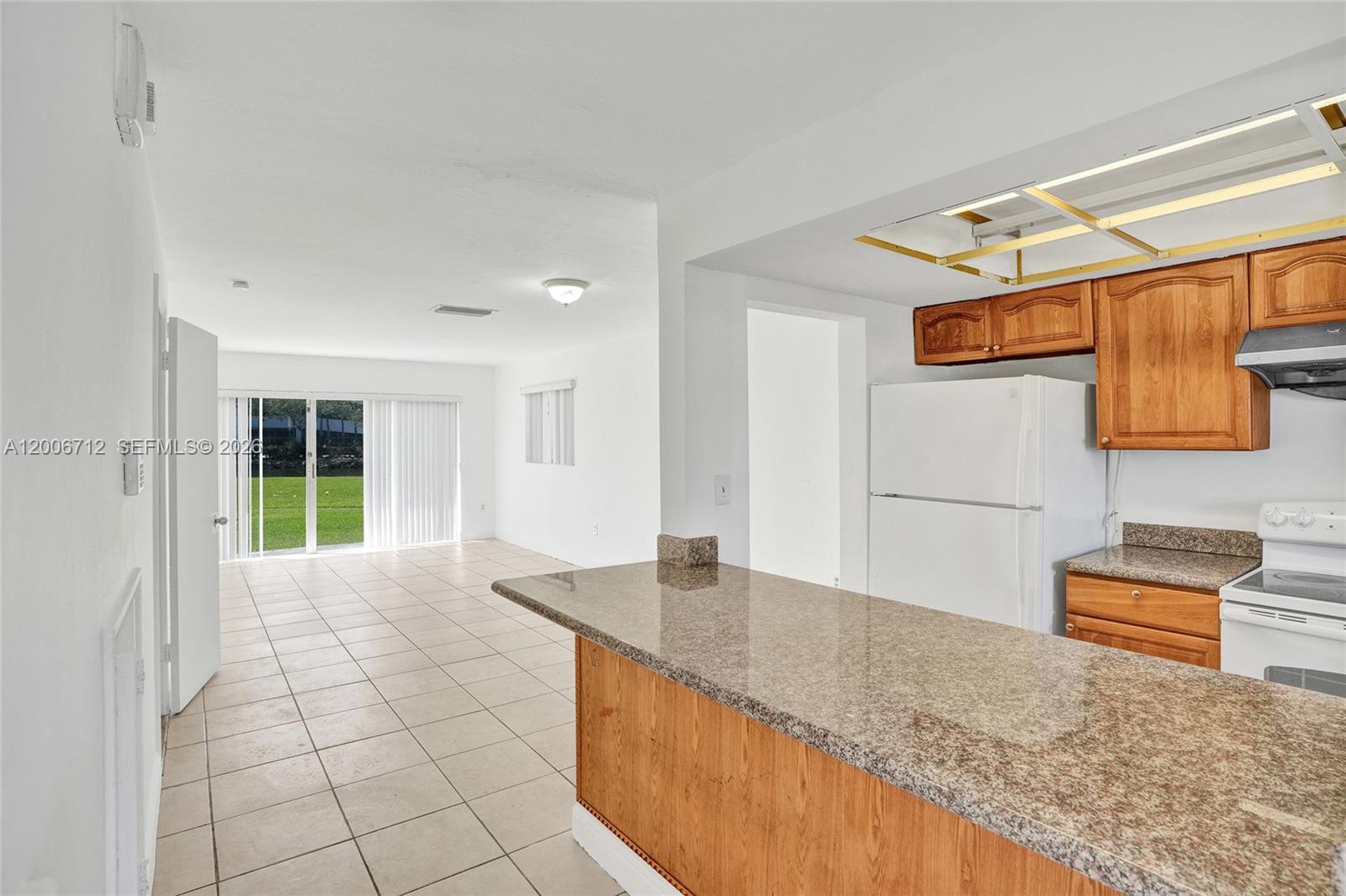 A kitchen with wood cabinets and granite countertops overlooks an open-concept living area with tile — 7344 SW 82nd St # C114, Miami FL 33143, MIAMI, FL
