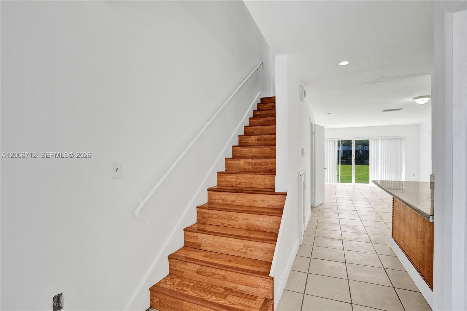 A wooden staircase with a white handrail sits beside a tiled room with sliding doors — 7344 SW 82nd St # C114, Miami FL 33143, MIAMI, FL