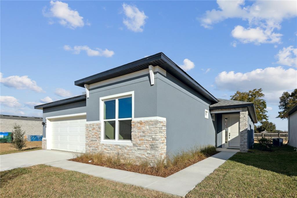 A single-story house with gray stucco, stone veneer accents, a white garage, and a walkway — 82 SPRINGWOOD DRIVE, PALM COAST, FL