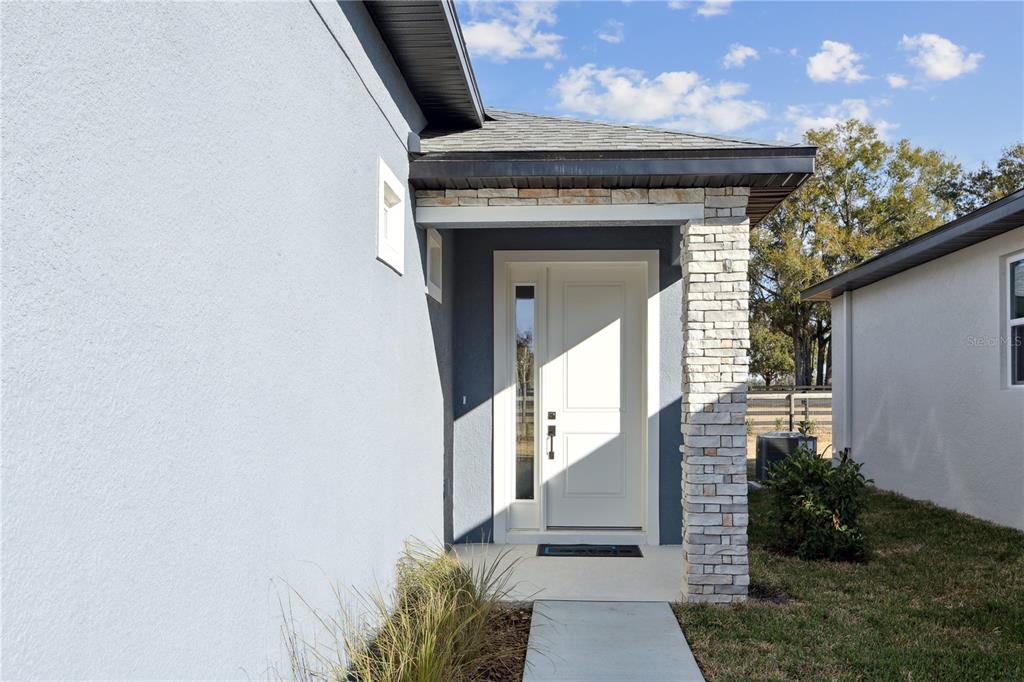 A modern home entrance features a white door with a sidelight and stone pillar accents — 82 SPRINGWOOD DRIVE, PALM COAST, FL
