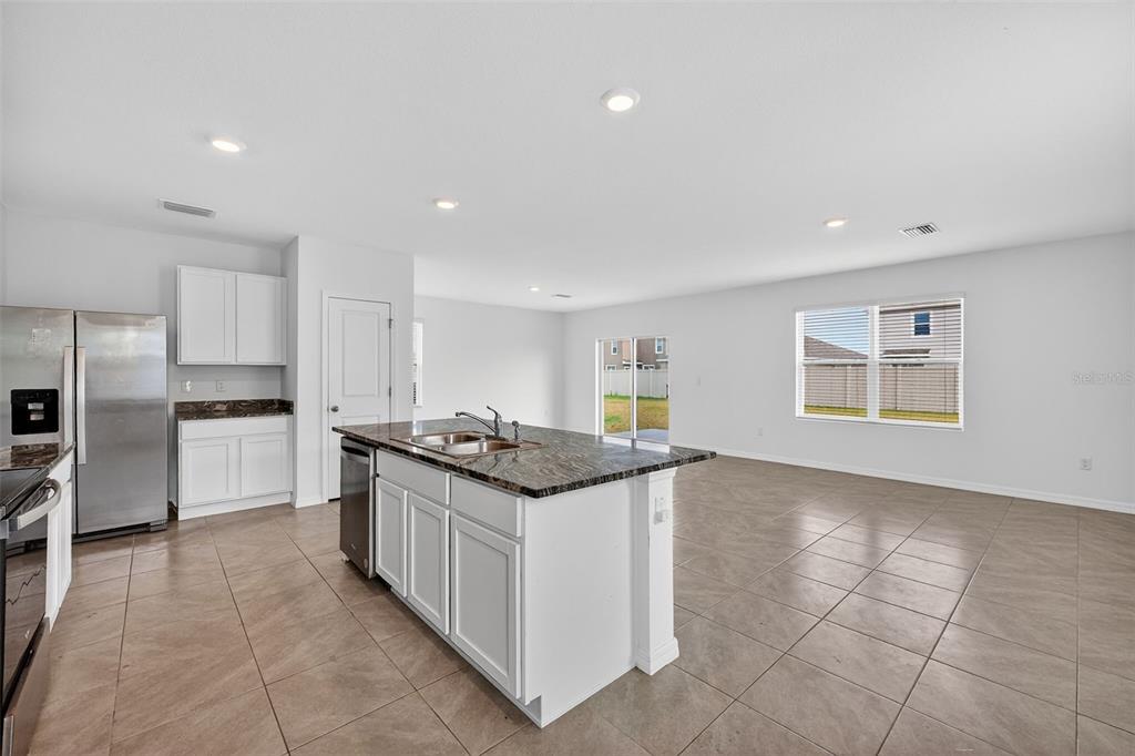 An open-concept kitchen with white cabinets, a granite island, and tile flooring — 3842 SUNNY SPRING STREET, PLANT CITY, FL
