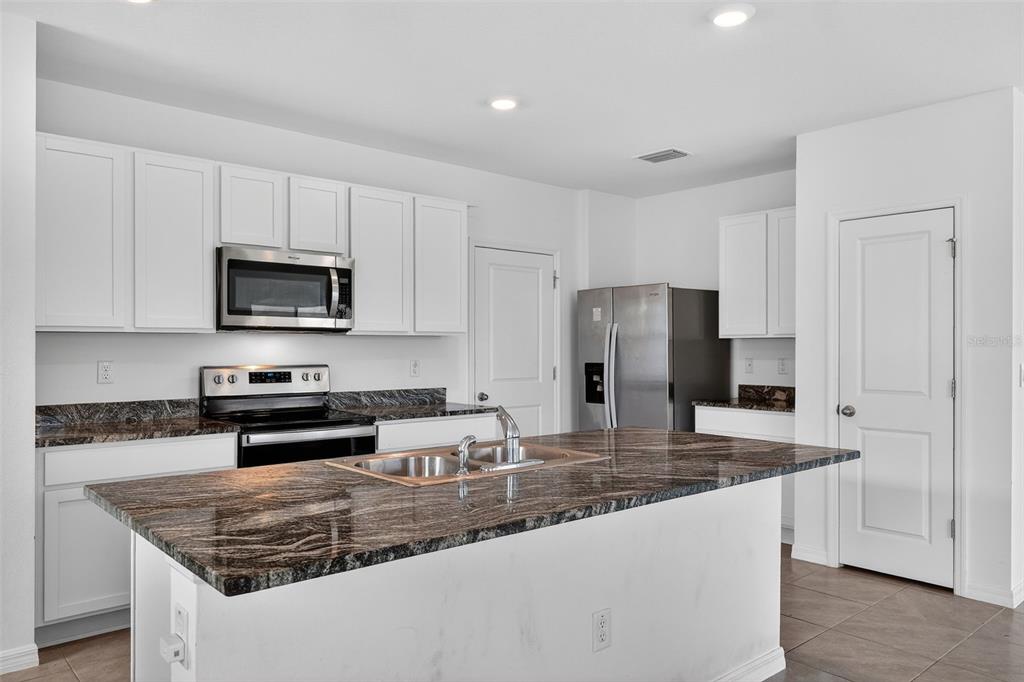 A kitchen features white cabinets, dark granite countertops, a center island, and stainless steel appliances — 3842 SUNNY SPRING STREET, PLANT CITY, FL