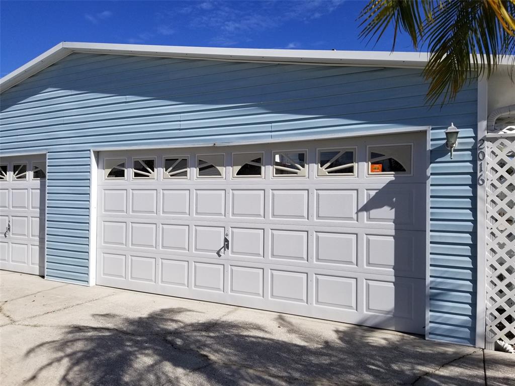 A blue-sided house features a two-car garage with white paneled doors and decorative windows — 2016 LAKE LINDA CIRCLE, LUTZ, FL