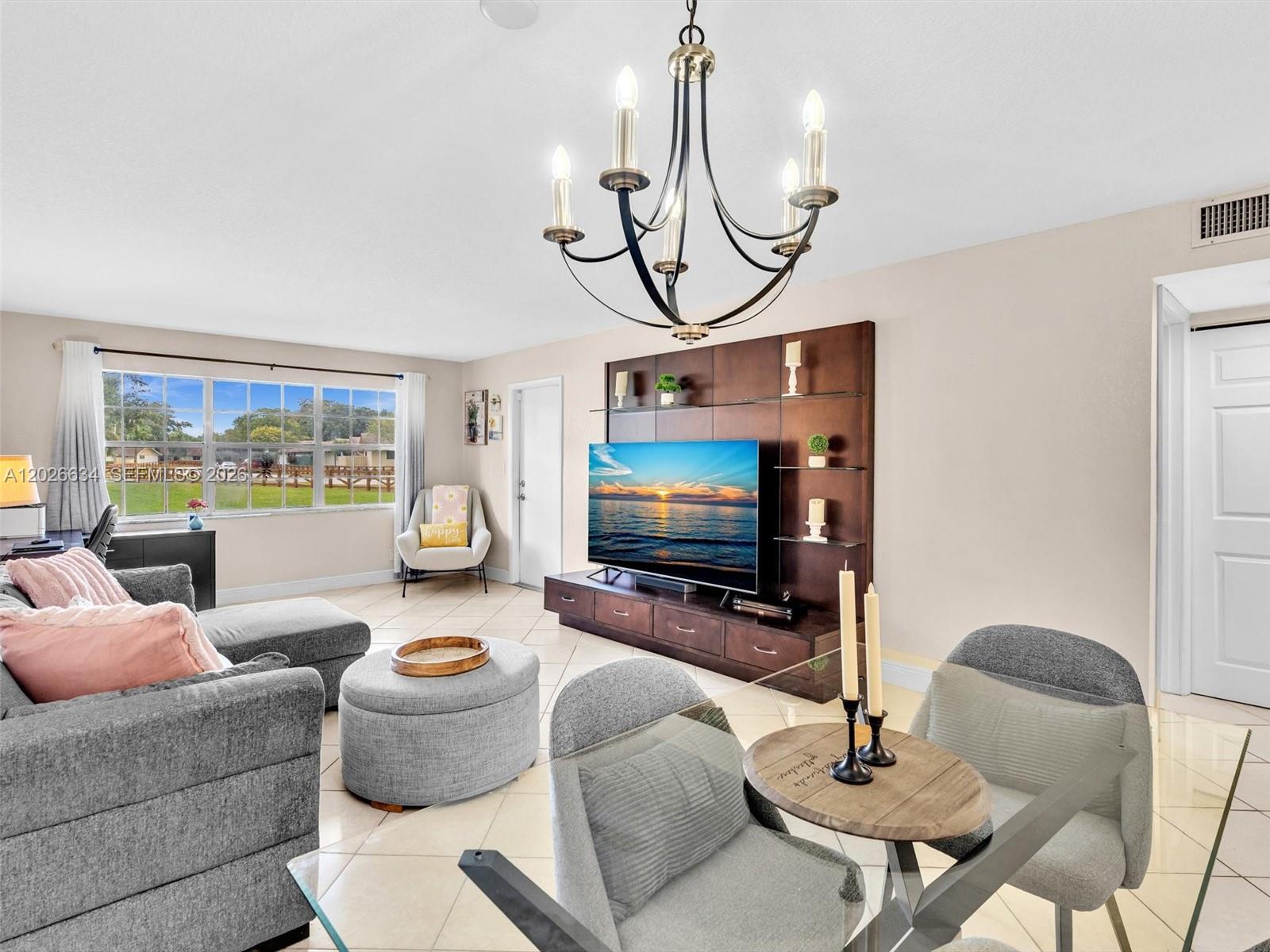 A living room features a grey sectional, a television on a dark wood unit, and a chandelier — 3660 Citrus Trce # 2, Davie FL 33328, DAVIE, FL