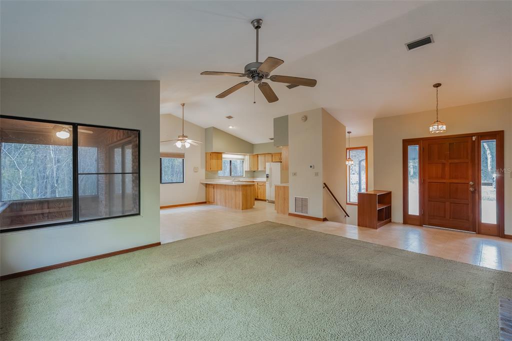 A living room with green carpet leads to an open kitchen with light wood cabinets — 1325 S SPRING GARDEN AVENUE, DELAND, FL