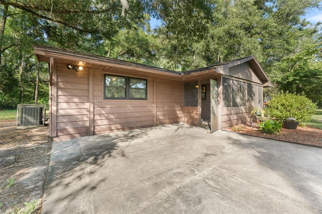 A brown wood-sided house features a concrete patio and a screened-in porch area — 79 NW 55TH AVENUE, BELL, FL