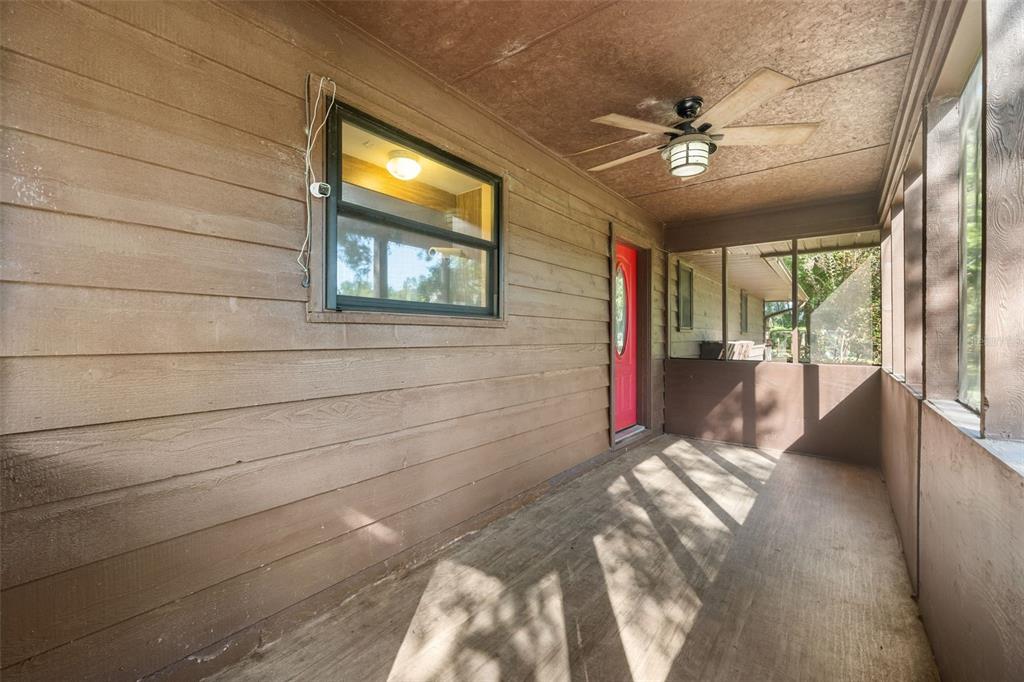 A covered wooden porch features a ceiling fan, a red door, and large screened windows — 79 NW 55TH AVENUE, BELL, FL