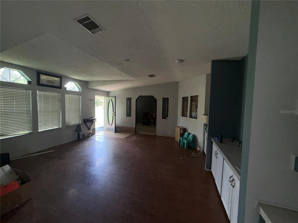 A spacious living area features wood-look flooring, white walls, and a doorway leading outside — 11316 MCMULLEN ROAD, RIVERVIEW, FL