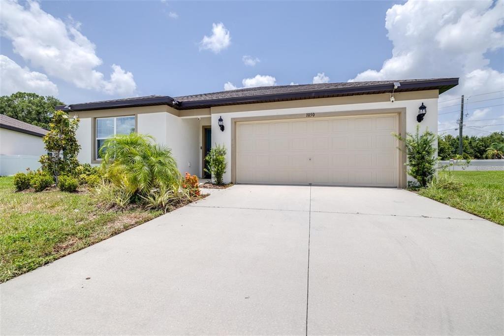 A single-story house with a beige stucco exterior, a two-car garage, and a concrete driveway — 1050 MICHELANGELO LANE, WINTER HAVEN, FL