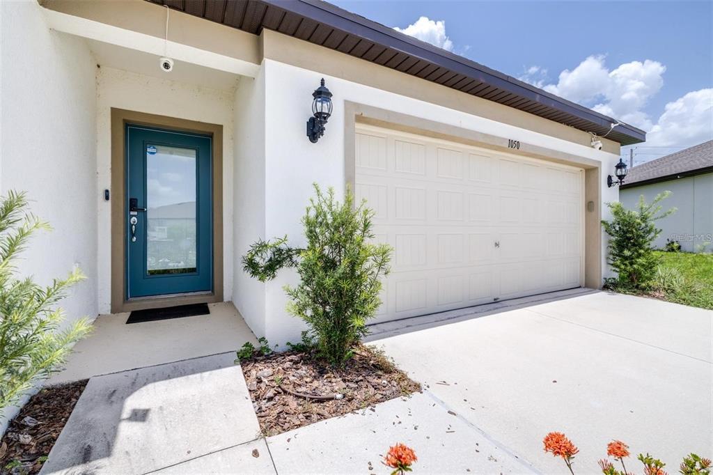 A white house exterior features a teal front door and a two-car garage — 1050 MICHELANGELO LANE, WINTER HAVEN, FL